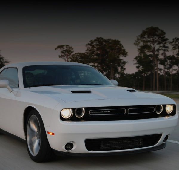 White Dodge Challenger on a road with trees in the background