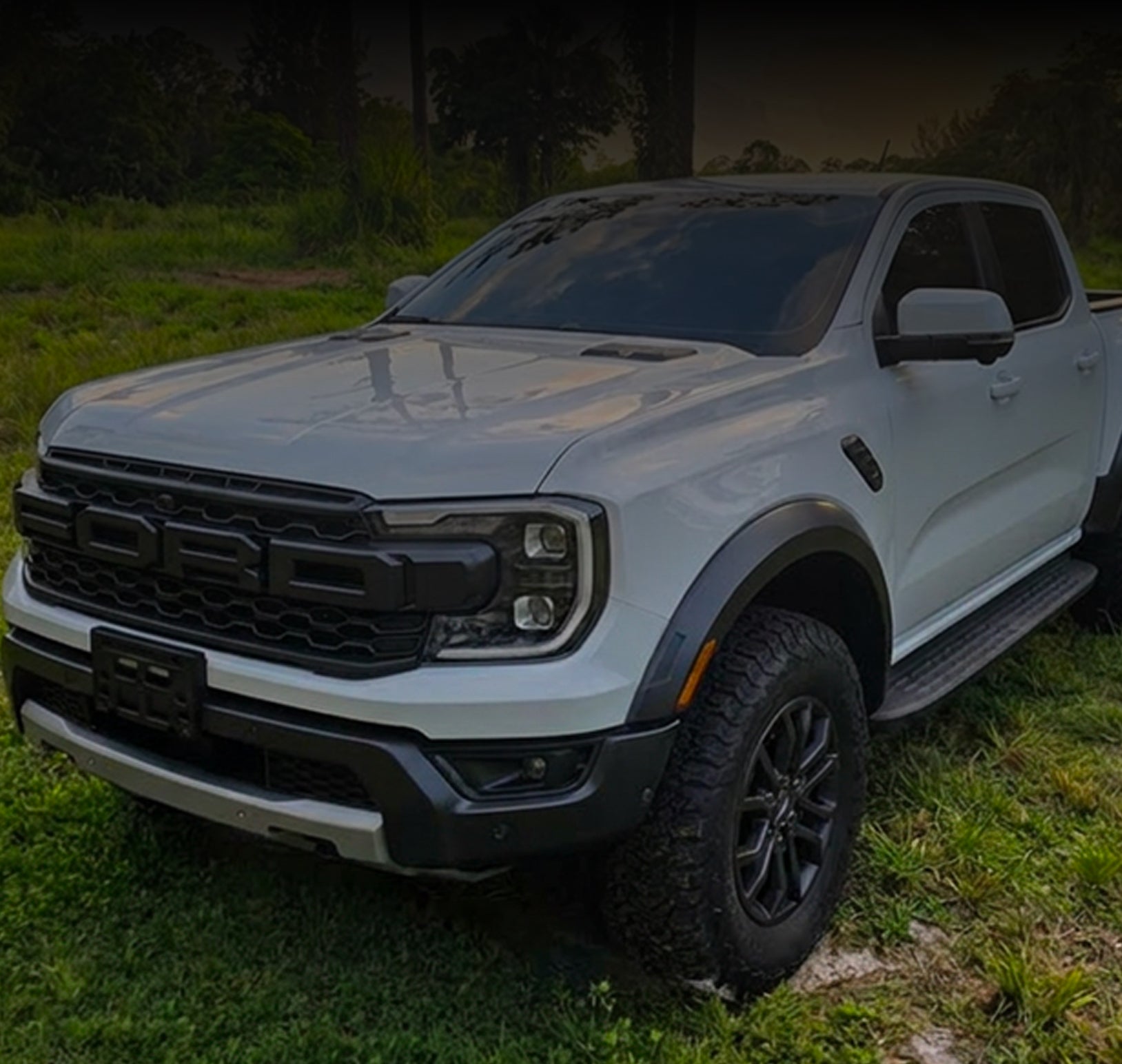 White Ford Ranger Raptor truck parked on grass with a dark background