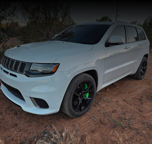 A white Jeep Grand Cherokee SRT off-road SUV parked on a dirt trail, featuring black wheels with bright green brake calipers.
