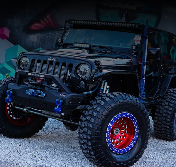 Black JK Wrangler off-road Jeep with large tires and colorful rims on a dark background