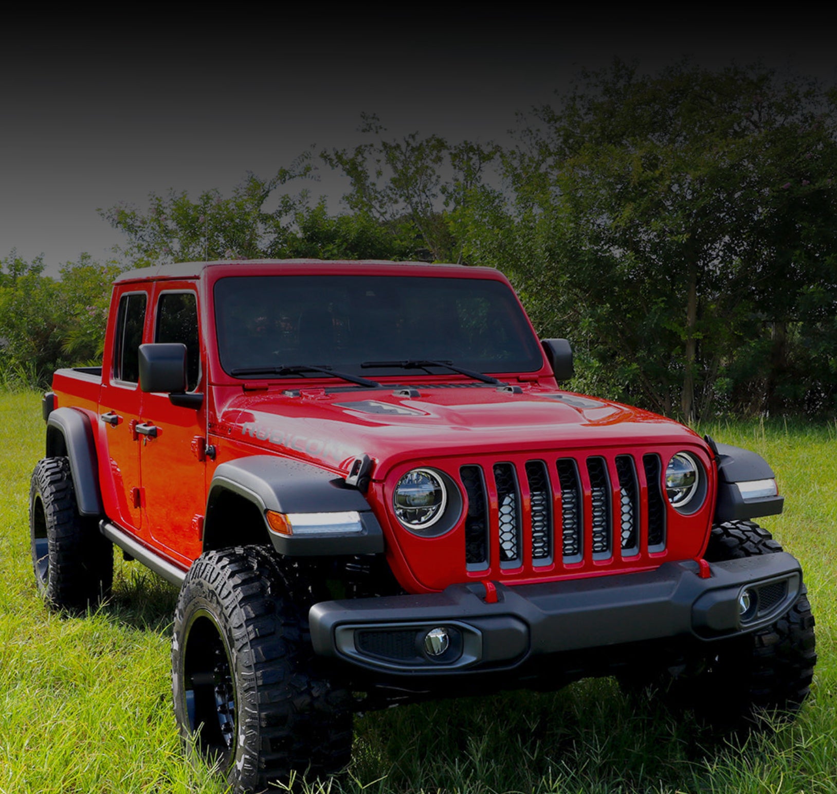 Red JT Gladiator Jeep truck parked on grass with trees in the background